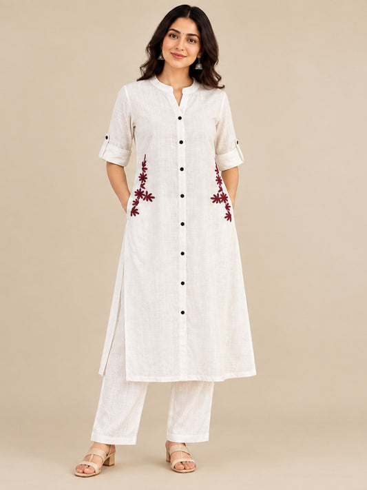 Woman wearing a white Cotton Flex kurta co-ord set with black buttons, roll-up sleeves and maroon floral embroidery near the side pockets