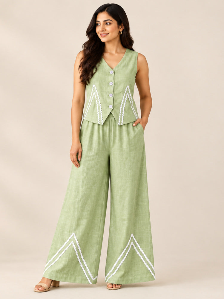 Woman wearing a sage green cotton flex co-ord set with a V-neck button-front waistcoat top and wide-leg pants with white rick-rack chevron trim